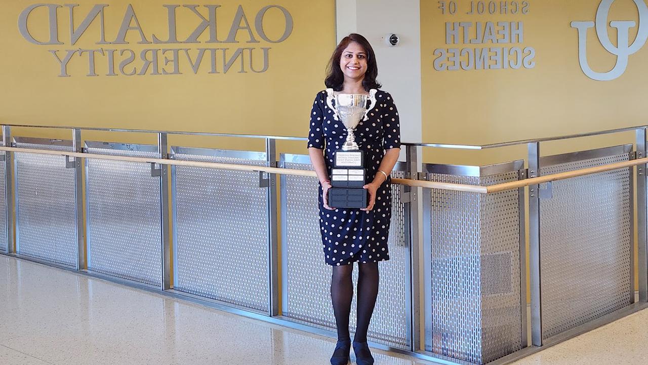 Woman stands in O U building holding a trophy.